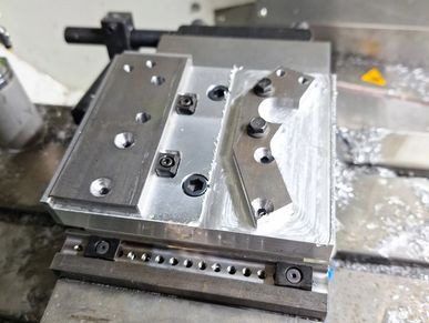 Metal part with screws and fixtures on a machining table.