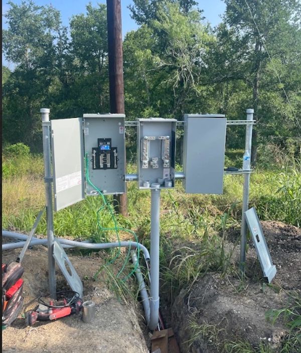 Electrical panels and wiring setup outdoors near a trench and greenery.