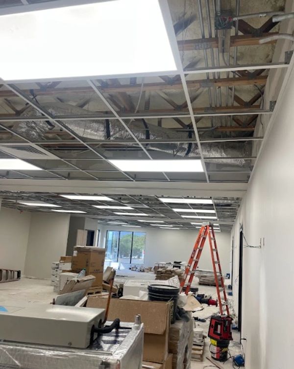 Office space under construction with ceiling panels missing and equipment scattered.