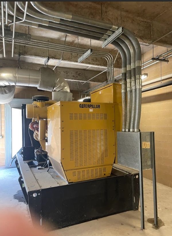 Yellow Caterpillar generator installed indoors with multiple conduits.