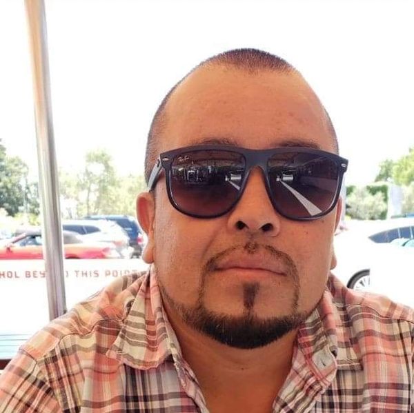 Man wearing sunglasses and a plaid shirt outdoors.