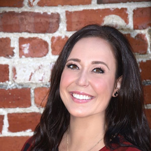 Smiling woman with dark hair in front of a brick wall.