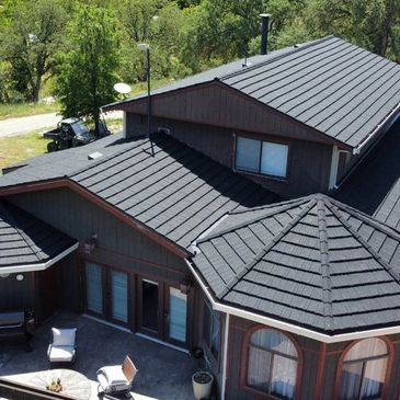 A modern house with a dark multi-gabled roof surrounded by greenery.