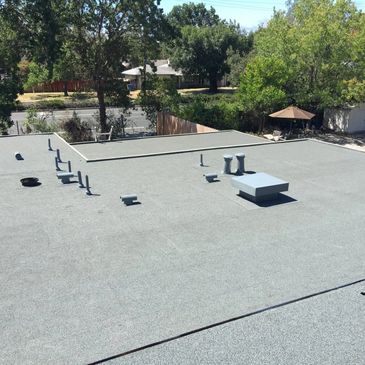 Flat rooftop with vents and pipes under sunny sky.