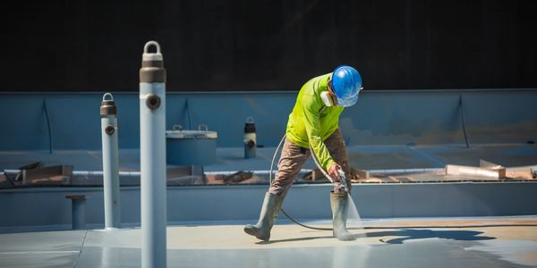 Worker in safety gear spraying a surface at a construction site.