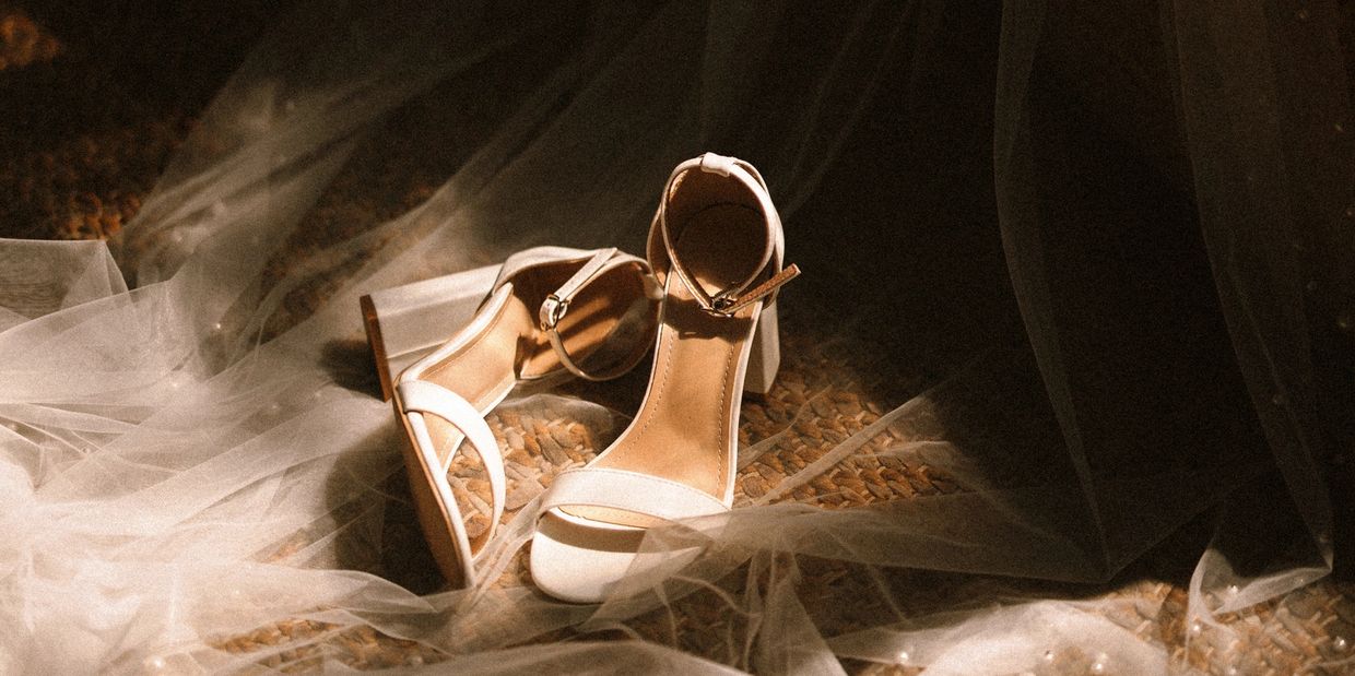Elegant beige high-heeled sandals on a textured surface with sheer fabric.