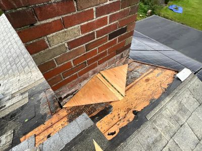 Roof repair work around a brick chimney.