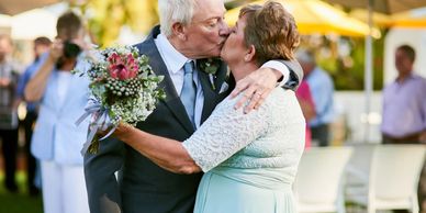 Elderly couple kissing at an outdoor wedding ceremony.