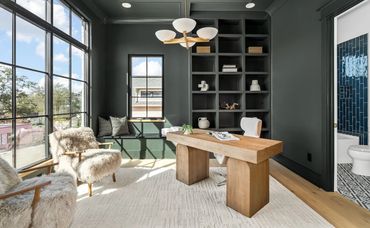 Modern home office with wooden desk and large windows.