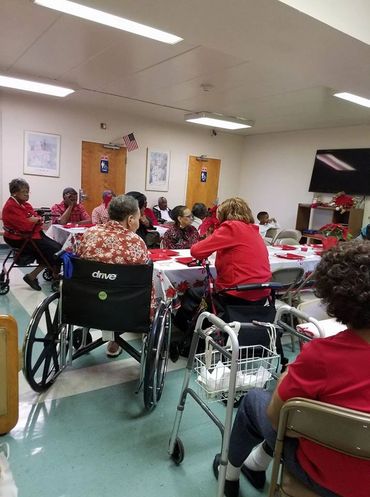 Seniors gathered in a community room, many wearing red and using mobility aids.