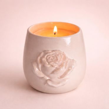 Lit candle in a white ceramic holder with a rose design.