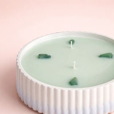 Round green candle in a white ribbed ceramic holder with decorative stones.
