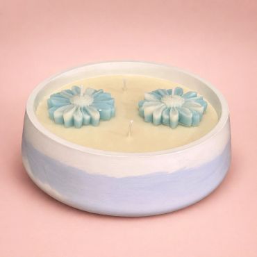 Round candle with blue flower-shaped wax decorations in a pastel holder.