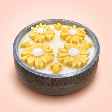 Round candle with yellow flower and bee designs in a gray holder.