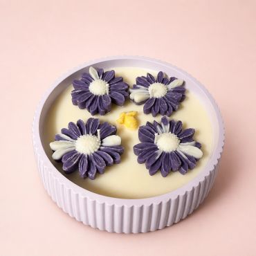 Decorative candle with four purple flower shapes and a small yellow bee in a round lavender holder.