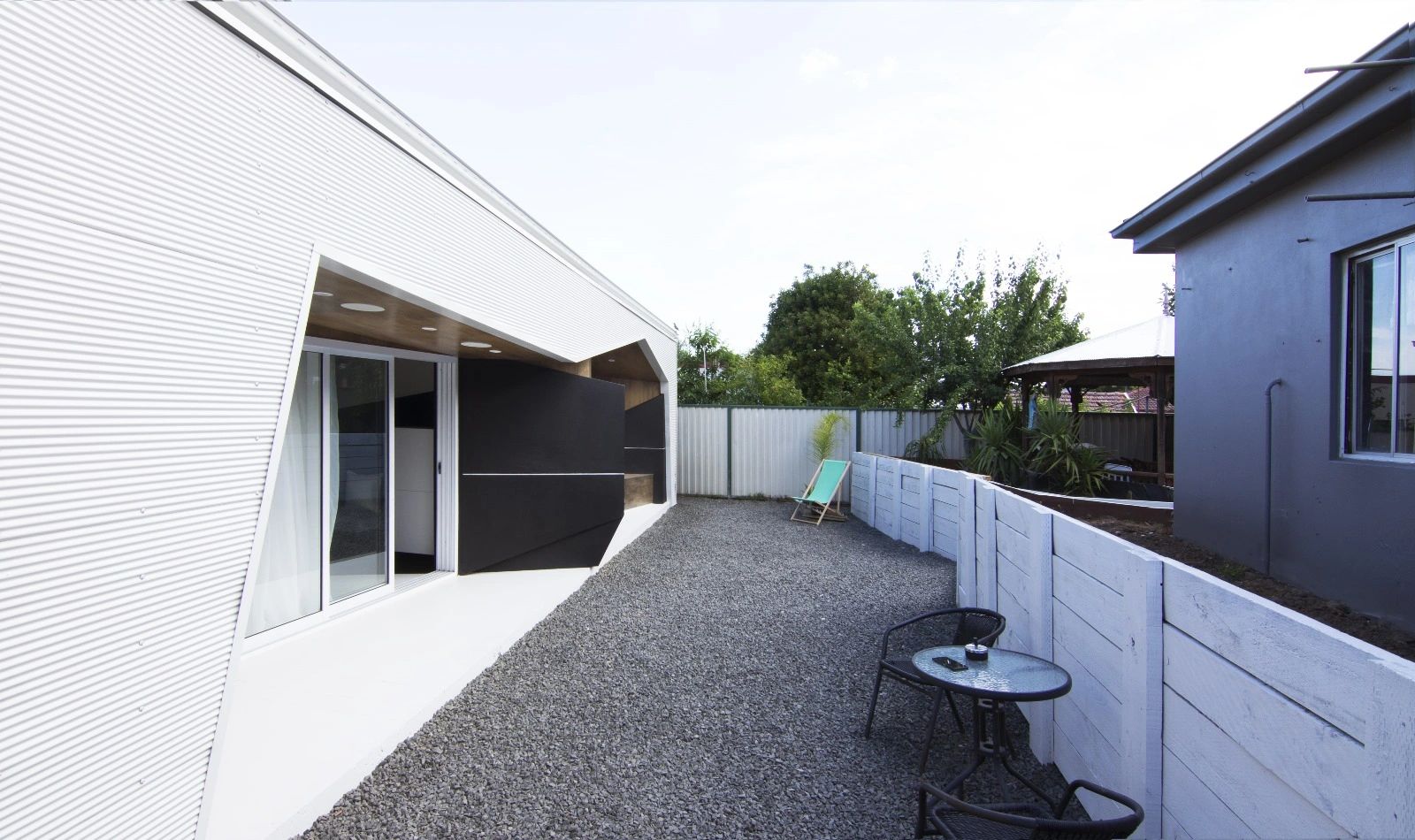 Modern backyard with gravel ground, white fence, and outdoor seating area.