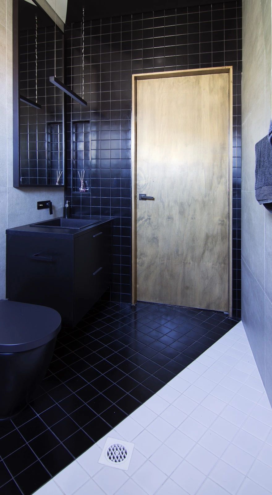 Modern bathroom with black tiles, wooden door, and minimalist fixtures.