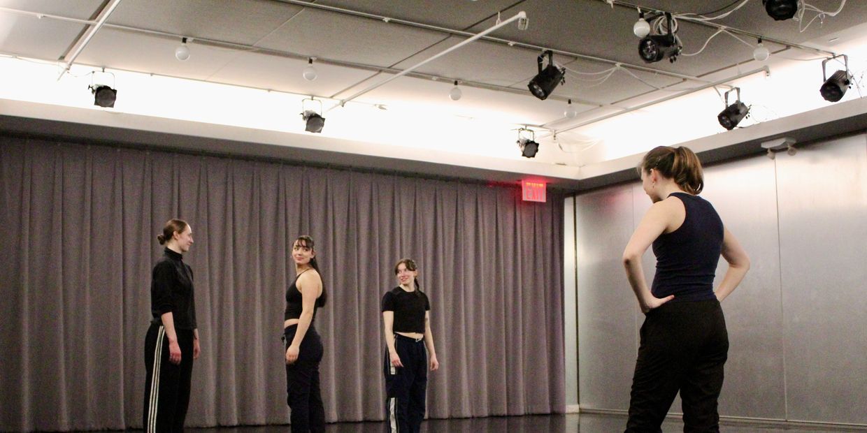 Four women in a dance studio engaged in a rehearsal or discussion.
