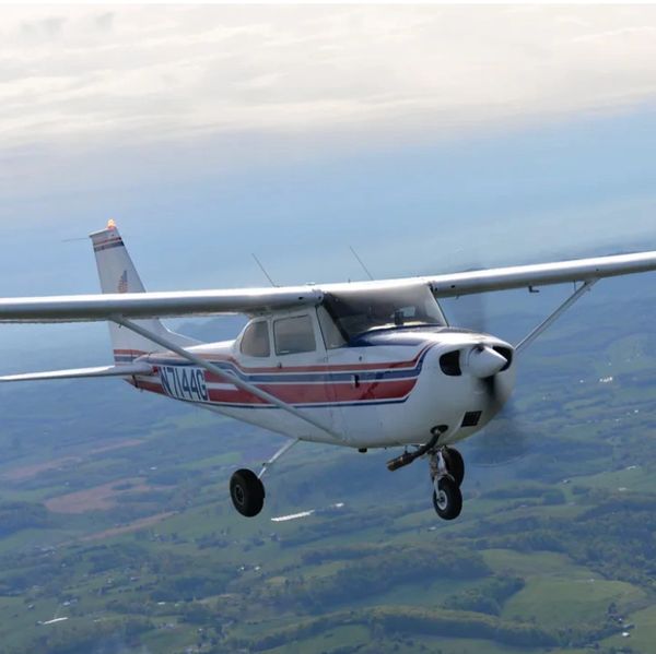 Single-engine plane flying over rural landscape.