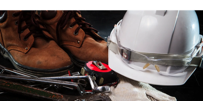 Work boots, safety helmet, gloves, and tools arranged on a black surface.