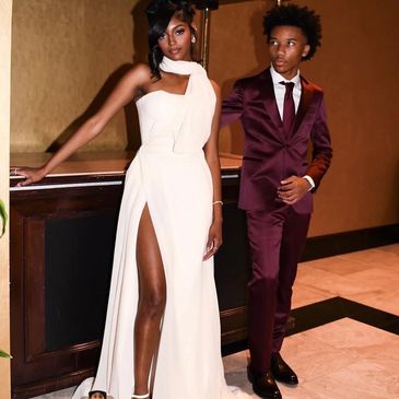 Elegant young woman in white gown with a young man in a burgundy suit.