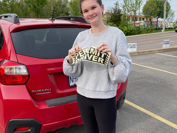 A girl standing behind a car tearing a paper from her hand