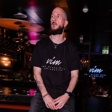Man sitting in a dimly lit bar wearing a black t-shirt.