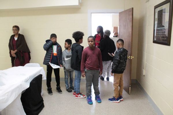 A group of children and adults standing in a room near a doorway.