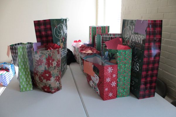 Christmas-themed gift bags arranged on a white table near a brick wall.