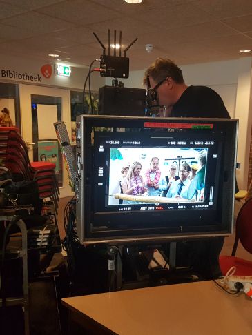Filming scene displayed on a monitor in a library setting.