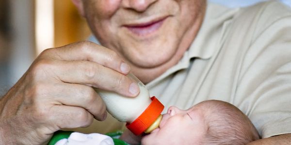 An elderly man lovingly feeding a baby with a bottle.