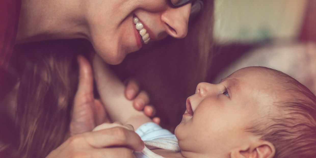 A smiling woman lovingly gazes at a baby in her arms.