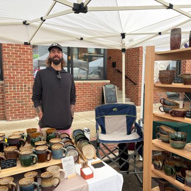 Man selling handcrafted pottery at an outdoor market booth.
