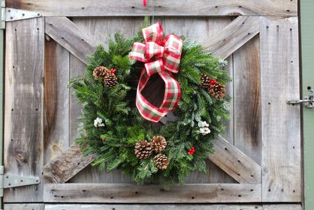 Festive Christmas wreath with pine cones and red plaid bow on wooden door.