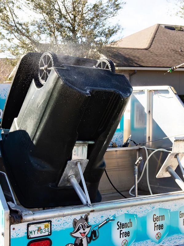 Worker power washing a trash bin on a mobile cleaning trailer.