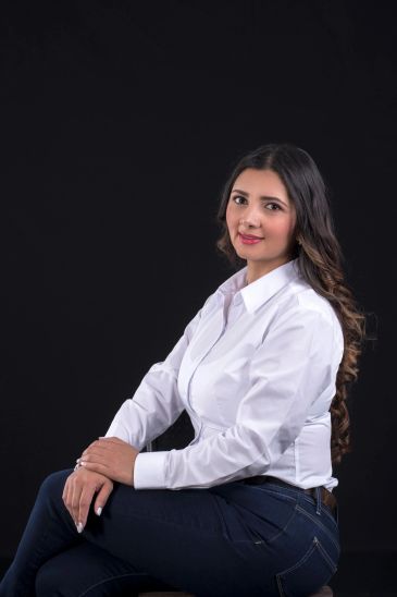 Mujer joven con camisa blanca y fondo negro, sonriendo.