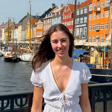 Smiling woman in white dress by colorful waterfront buildings.