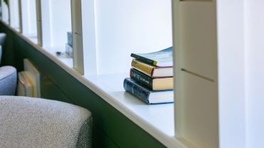 Stack of books placed on a white windowsill next to a cozy chair.