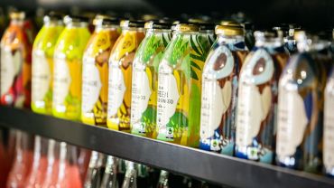 Colorful bottled drinks lined up on a store shelf.