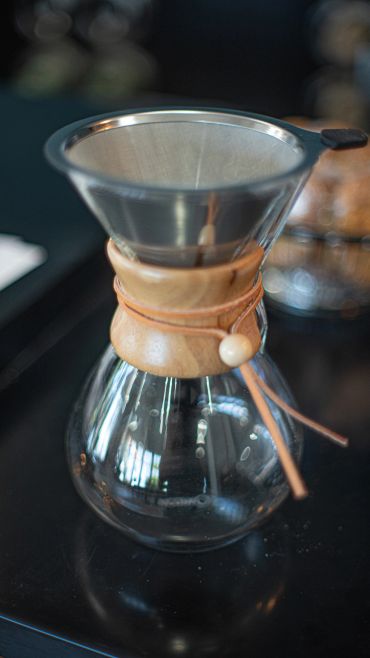 Glass coffee carafe with wooden collar and metal filter on a black surface.