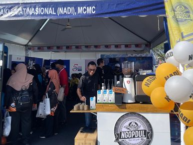 People gathered at a coffee stand with NADI and MCMC banners at an event.