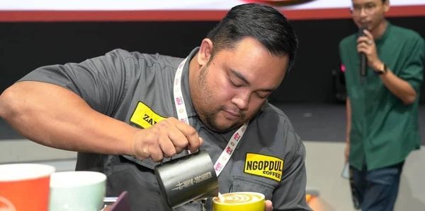 Barista skillfully pouring latte art into a cup at a coffee event.