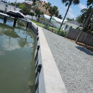 A waterfront area with a concrete seawall and gravel pathway beside calm water.
