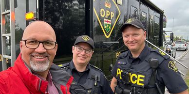 Three smiling men, including two police officers, pose for a selfie.
