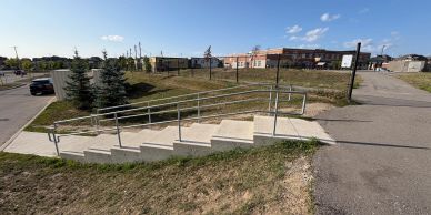 Sidewalk ramp with handrails beside steps in suburban area.