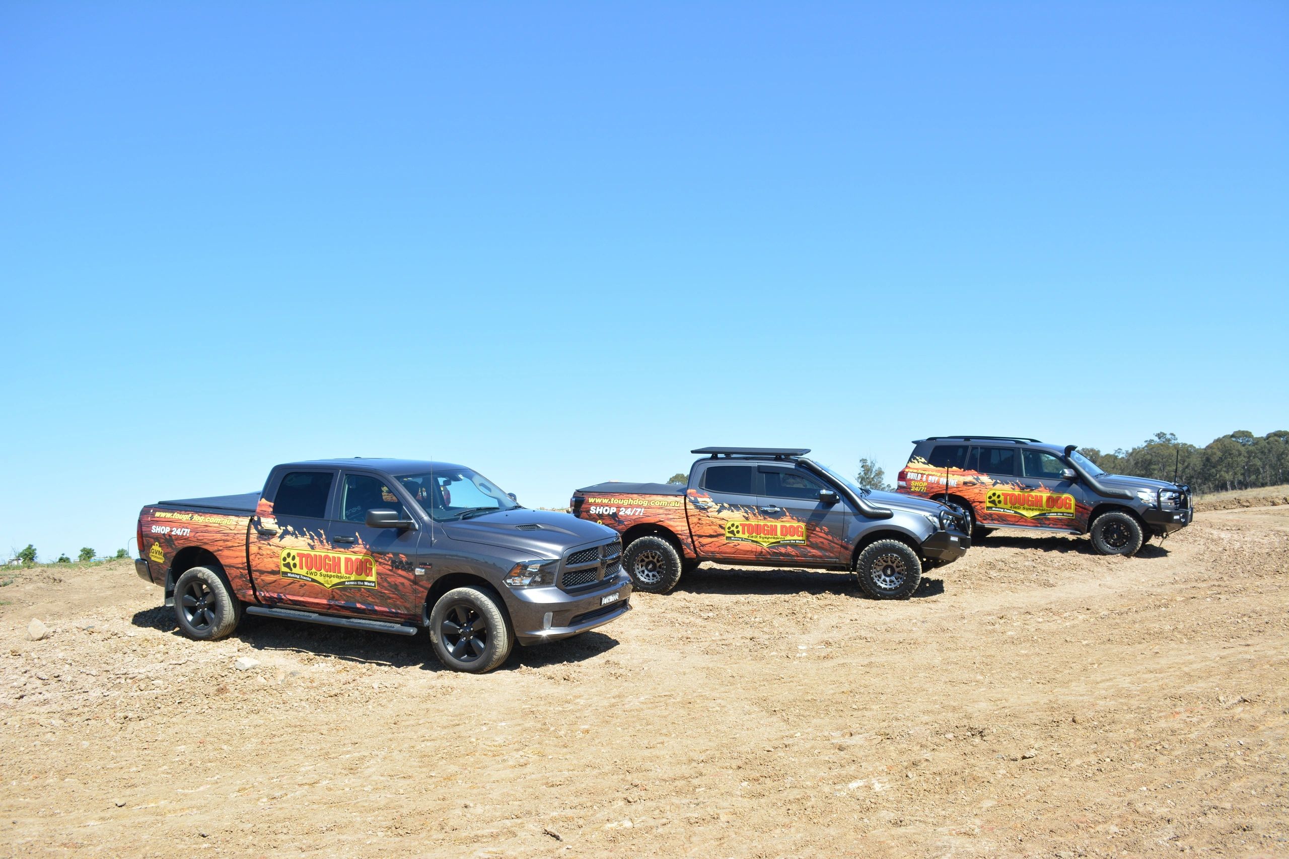 three 4wds park in paddock with tough dog sign writing and suspension