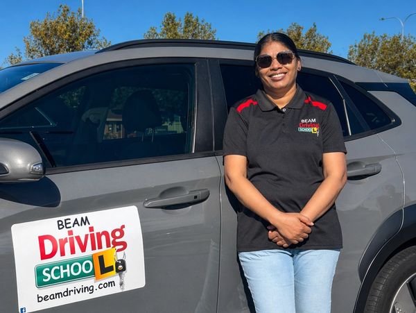 Smiling woman standing next to a BEAM Driving School car.