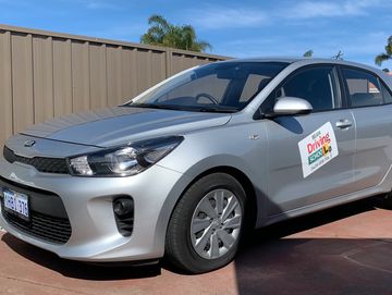 Silver Kia car with driving school signage parked outside.