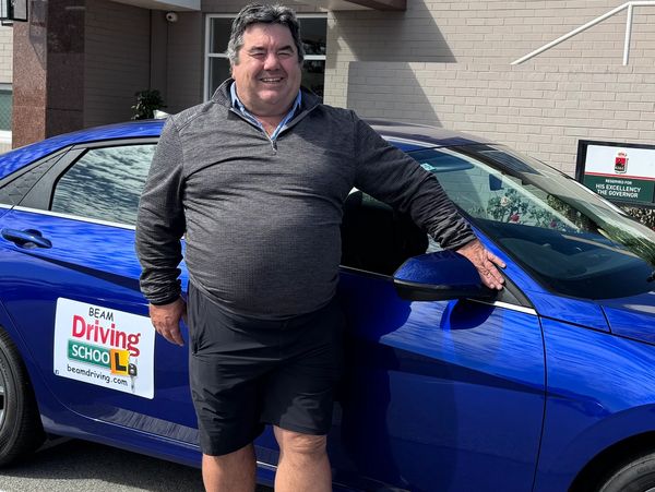 Man smiling next to a blue car with a driving school sign.