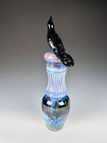 A ceramic vase with a black bird sculpted on top.